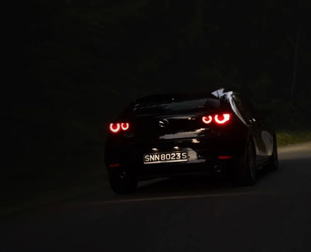 Black car with glowing taillights on a dark road.