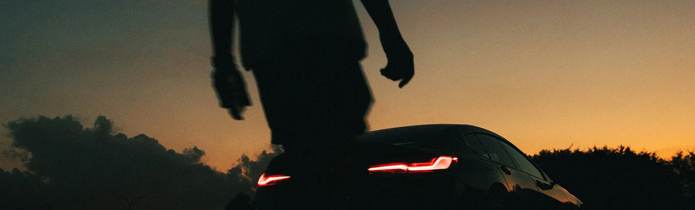 Silhouette of a person near a car at sunset.