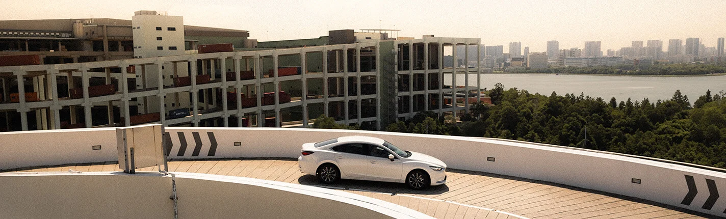 White sedan on a curved rooftop road, cityscape and greenery in the background.