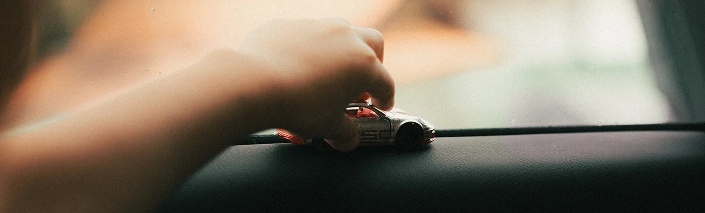 Child's hand holding toy car on dashboard.