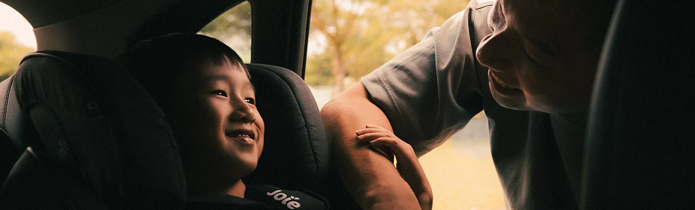 Parent smiling at a child in a car seat, enjoying a moment of connection.