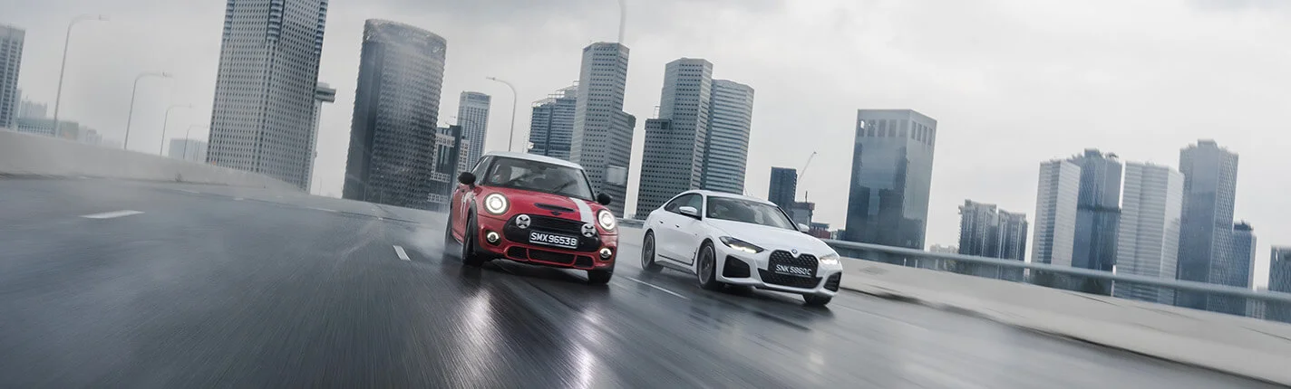 Red Mini Cooper and white BMW driving on a rainy urban highway.